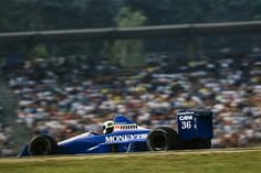 a man driving a blue race car on top of a grass covered field in front of a crowd