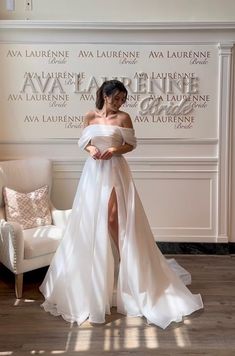 a woman standing in front of a white couch wearing a dress with high slits