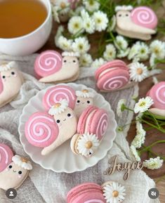 pink and white decorated cookies sitting on top of a plate next to a cup of tea