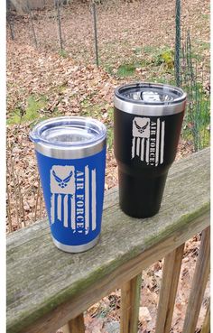 two tumblers sitting on top of a wooden rail in front of a wooded area