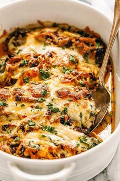 a white casserole dish with cheese and spinach on top, topped with a serving spoon