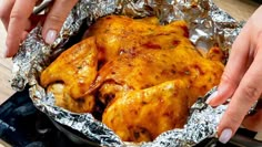 two hands holding a chicken in foil on top of a stove