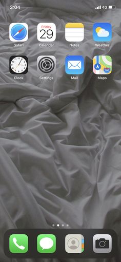 an iphone with icons on the screen is laying on a bed covered in gray sheets