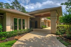 a driveway leading to a house with lots of trees in the front yard and bushes on either side