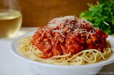 a white bowl filled with spaghetti and sauce next to a glass of wine on a table