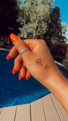 a woman's hand with a small butterfly tattoo on her left wrist, next to a swimming pool