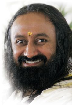 a man with long hair and a beard wearing a yellow flower on his forehead smiles at the camera