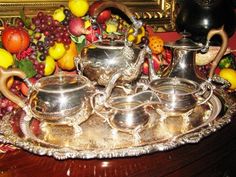 a silver tea set sitting on top of a wooden table next to fruit and flowers