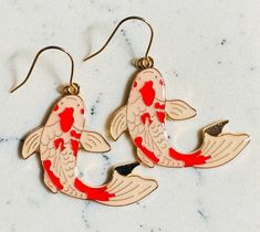 two gold and red koi fish earrings sitting on top of a marble countertop