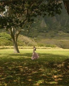 a woman standing under a tree on top of a lush green field