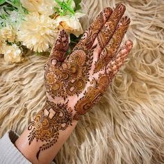 a woman's hand with henna on it and some flowers in the background