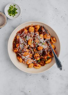 a white bowl filled with pasta and sauce on top of a marble table next to two bowls