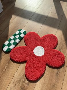 a red flower rug sitting on top of a wooden floor next to a green and white object