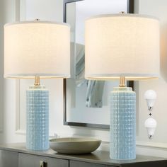 two blue lamps sitting on top of a table next to a mirror and lamp shade