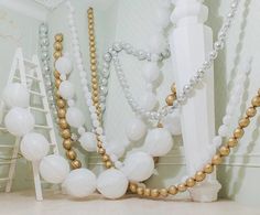 white and gold balloons are hanging from the ceiling in an elegant room with ladders