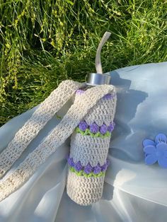 a crocheted bottle cover sitting on top of a white sheet next to a blue butterfly