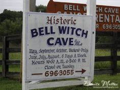 a sign for bell witch cave in front of a wooden fence with two signs behind it