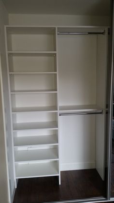 an empty walk - in closet with white shelves and open doors, next to a hardwood floor