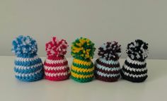 several small knitted objects are lined up in a row on a table, one has a pom - pom