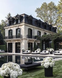 a large house with a pool in front of it and lots of white flowers on the lawn