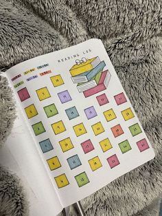 an open book sitting on top of a pile of gray fuzzy material with colorful squares