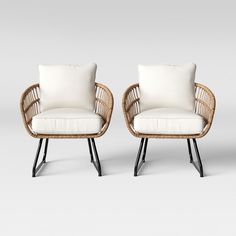 two wicker chairs with white cushions and black legs, one is facing the other