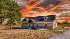 a house sits on the side of a dirt road in front of an orange sunset