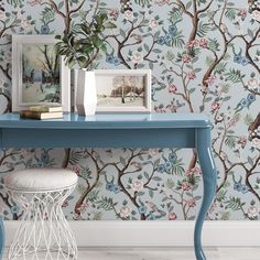 a blue table with two pictures on it next to a white stool and wallpaper