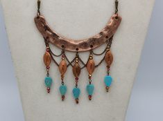 "This unique handmade statement necklace features a curved copper finish hammered bar component accented by drops created with ornate vintage copper beads, faceted copper/pink/gold crystal rondells and ending with textured turquoise magnesite stone leaves. The whole design is brought together with a subtle backdrop of copper link chain \"netting\" and is finished with custom copper lantern chains and a lobster clasp closure. This extraodinary piece comes complete with matching earrings, which me Bronze Copper Jewelry With Dangling Beads, Copper Jewelry With Dangling Beads, Bohemian Copper Necklace With Patina, Unique Copper Jewelry With Dangling Beads, Textured Turquoise, Diy Statement Necklace, Handmade Statement Necklace, Copper Lantern, Copper And Pink