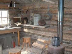 an old log cabin with wood burning stove and wooden stools in the foreground