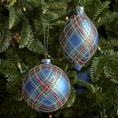 two ornaments hanging from a christmas tree with lights in the background and plaid fabric on them