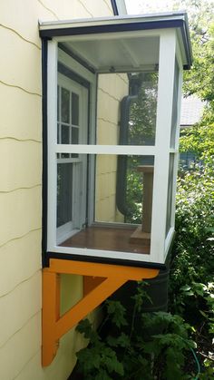 an open window on the side of a house in front of some trees and bushes