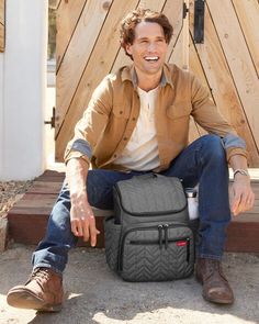 a man sitting on the ground with a backpack in his lap and smiling at the camera