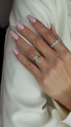 a woman's hand with pink manicured nails and two diamond rings on it