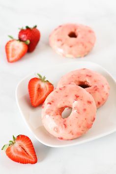 two donuts on a plate with strawberries next to them