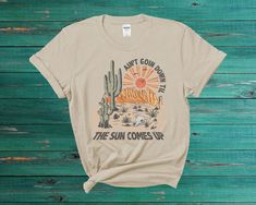 Get ready to rock the summer with our Desert Western Summer T-Shirt. This vintage-inspired tee features a bold graphic print of a desert landscape, complete with a classic Western font. Crafted from high-quality, soft materials, this tee is designed for both comfort and durability. The classic fit and unisex design make it a versatile addition to any wardrobe. The vintage-inspired graphic and muted colors give it a unique, retro feel, perfect for both casual and dressy occasions. Whether you're hitting the beach or just lounging at home, this Desert Western Summer T-Shirt is the perfect choice for summertime fun. The breathable fabric is perfect for warmer weather, and the high-quality construction ensures that it will hold up to wear and tear over time. This vintage Summer Graphic T-Shirt Summer Adventure T-shirt With Text Print, Vintage Summer Outdoor T-shirt, Summer Outdoor T-shirt With Front Print, Relaxed Fit T-shirt For Summer Adventure, Summer Adventure Graphic Print T-shirt, Western Summer, Vintage Desert, Western Font, Summer Tshirt