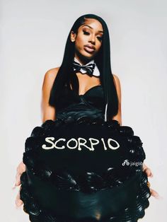 a woman holding a large black cake with the word scorpio written on it