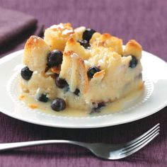 a piece of bread pudding with blueberries on it and a fork next to it