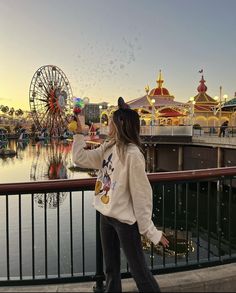 a woman standing on the edge of a pier next to a ferris wheel