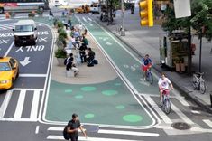 people are walking and riding bikes on the street in an intersection with green painted markings