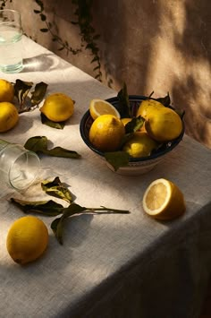 a table with lemons and water on it next to a bowl full of lemons