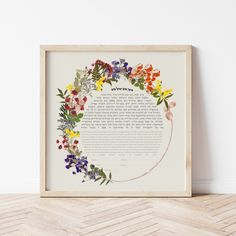 a framed paper with flowers on it in front of a white wall and wooden floor