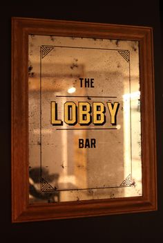 the lobby bar sign is reflected in an old glass window with rusted wood frame