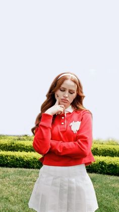 a girl in a red shirt and white skirt is posing for the camera with her hand on her chin