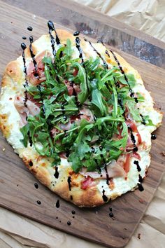 a pizza topped with greens on top of a wooden cutting board