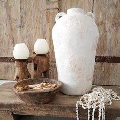 a white vase sitting on top of a wooden table next to a bowl and lamp