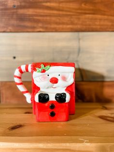 a red and white santa claus mug sitting on top of a wooden table