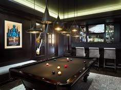 a pool table in the middle of a room with chairs and bar lights hanging from the ceiling