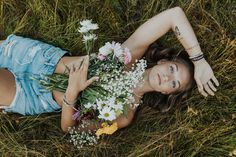 a woman laying on the grass with flowers in her hand and looking at the camera