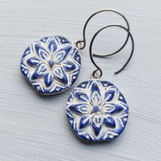 two blue and white earrings with circular designs on them sitting on top of a wooden table